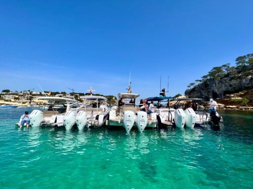 Mehrere Trainingsboote mit Teilnehmern laengsseits zusammengebunden in einer tuerkisfarbenen Bucht bei Mallorca
